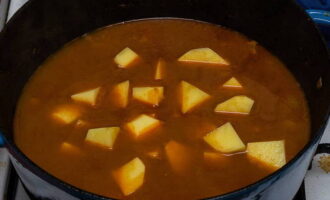 Corta las patatas en cubos, agrégalas a la carne y añade agua para que cubra el contenido de la sartén.