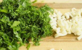 Without wasting time, prepare the dressing: pass the garlic through a press and finely chop the greens.