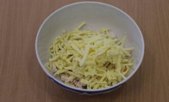 A piece of hard cheese is crushed using a coarse grater and placed on top of the chicken pieces.