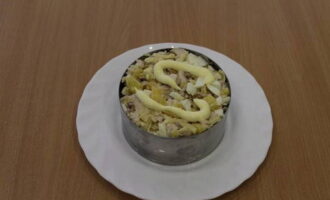 The prepared salad is placed into portioned plates using small rings. Each serving of salad is topped with a little mayonnaise and sprinkled with chopped nuts.