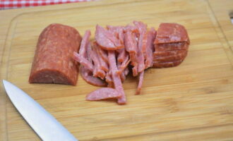 Hunter's salad with smoked sausage is very easy to prepare. Take a loaf of sausage and cut off the required amount with a sharp knife. We release a piece of the ingredient from the shell. Place the sausage on a cutting board and thinly slice into strips.