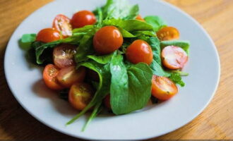 Kirschtomaten waschen, halbieren und auf die Rucolablätter legen.