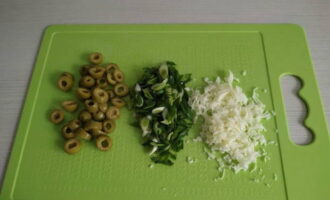 Grind a piece of hard cheese using a grater, finely chop the green onions, and cut the pitted olives into rings.