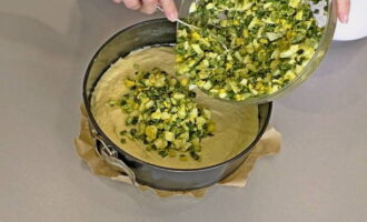 The baking dish is covered with parchment paper and greased with oil. Half of the kneaded dough is poured into the mold. The onion filling is laid out on top of it in an even layer.