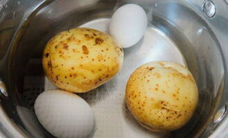 Gleichzeitig die gewaschenen Kartoffeln in der Schale kochen. Hühnereier hart kochen. Die gekochten Zutaten schnell in kaltem Wasser abkühlen lassen.