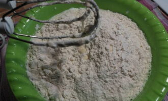 Ayak tepung melalui penapis. Kemudian tuangkan dalam bahagian kecil ke dalam asas cecair dan segera menguli doh.