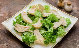 Preparate un piatto sul quale raccoglierete l'insalata. Sciacquare e asciugare le foglie di lattuga. Foderare una pirofila e adagiarvi sopra le fettine di pollo tagliate a pezzetti.