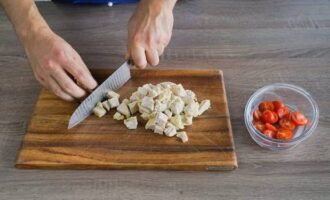 Corta el filete de pollo cocido y enfriado en cubos. Enjuagar 200 gramos de tomates cherry, secarlos y cortarlos por la mitad a lo largo.