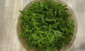 L'insalata con gamberi e rucola è molto facile da preparare. Dividere 100 grammi di rucola, metterli in uno scolapasta o in un colino e sciacquare abbondantemente sotto l'acqua. Asciugare le foglie, strapparle con le mani se necessario e disporle su un piatto da portata.