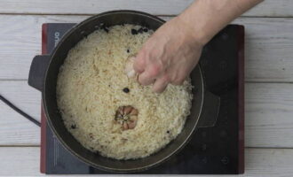 Assim que a água for absorvida pelo arroz, mergulhe as cabeças de alho até a metade no arroz.Reduza o fogo para médio, cubra com uma tampa e cozinhe o pilaf até ficar cozido.