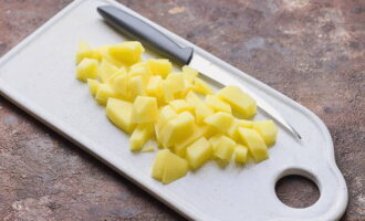 Descasque as batatas, enxágue e corte em cubinhos, coloque numa panela com as ervilhas cozidas e cozinhe por mais 20 minutos.