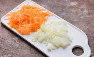 Enquanto a sopa cozinha, corte a cebola descascada em cubinhos e pique as cenouras num ralador grosso. 