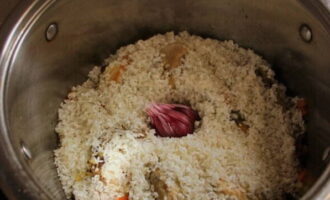 Pour rice into the pan. Distribute it evenly. Sprinkle with spices for pilaf and insert a head of garlic into the center, from which we first remove the top husk.