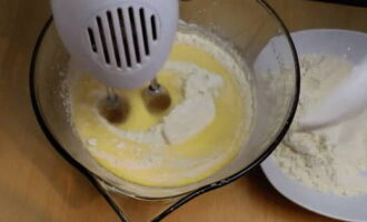 Sift the flour into a sieve. Without turning off the mixer, pour the flour into the beaten eggs in portions and knead the dough until smooth. Turn on the oven to 180°C.