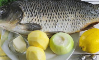 La carpe cuite au four est très simple à préparer. Rassemblez les ingrédients nécessaires pour un plat élégant. Retirez la peau des pommes de terre à l'aide d'une aide ménagère. Libérez les ampoules de la couche supérieure. Rincez et séchez le citron.