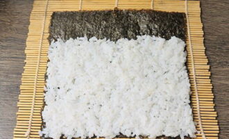 Place a sheet of nori on the mat, smooth side down, spread the rice with wet fingers, leaving no gaps, going out two centimeters on one side and not reaching the opposite side. 