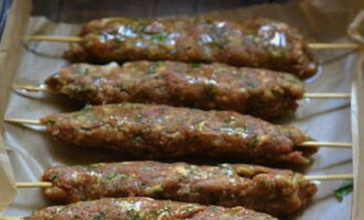 Place the minced meat on wooden skewers pre-soaked in water, distributing it along the length of the skewers. Place the skewers on a baking sheet lined with parchment paper or foil. Turn on the oven to preheat, setting the sensor to 180 degrees.