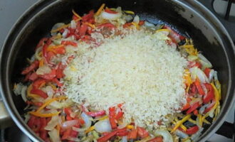 Numa frigideira aqueça o azeite e frite as cenouras e as cebolas até ficarem macias. Em seguida, adicione os pimentões picados e frite por mais alguns minutos. Lave o arroz várias vezes em água fria, junte aos legumes e frite até que os grãos fiquem saturados de óleo e fiquem transparentes.