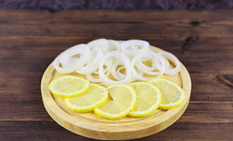 Skålla citronen med kokande vatten, torka, skär i skivor. Skär den skalade löken i inte för tunna ringar.