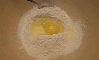 First, let's prepare the dough. Sift flour into a deep bowl.Break a chicken egg into it and pour in water, previously mixed with salt.