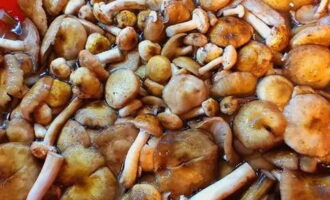 Sort out honey mushrooms from forest debris. Place in a large container and fill with water. The specks will float up. Use a slotted spoon or sieve to collect them. Rinse until the water runs clear.