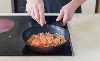 Add tomato pieces and chopped basil to the onion. Salt the contents and sprinkle with ground black pepper. Simmer the vegetables until the liquid evaporates.