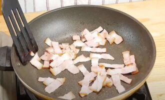 Metti la pancetta tritata in una padella riscaldata e friggi fino a quando diventa leggermente dorata.