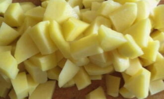 We wash the potatoes and remove the peels using a housekeeper. Cut into cubes. At the same time, put a pan of water to heat up.