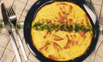 Cover the frying pan with a lid. Fry the omelette over low heat for 5-7 minutes until cooked. Then sprinkle it with herbs. Fold the fluffy omelette with milk and sausage prepared in a frying pan in half, transfer to a plate and serve the dish immediately to the table. Bon appetit!