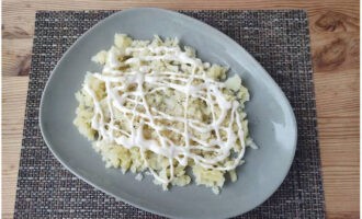 Bedecken Sie die Kartoffelschicht mit einem dünnen Netz Mayonnaise.