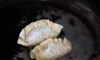 We pinch the edges tightly, giving the semi-finished products an oblong shape. Place the dumplings in a frying pan with heated vegetable oil and fry for 2 minutes, then pour in ½ cup of water and keep covered until the liquid has evaporated.