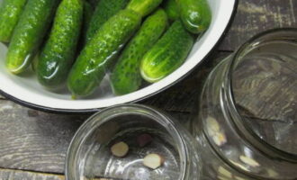 How to hot pickle cucumbers for the winter? Let's prepare the necessary ingredients. Pre-soak the cucumbers in cold water for 8 hours. This will make the vegetable crispy. We sterilize the jars. Place pieces of garlic in them.