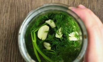 Legg hvitløksskiver og en forhåndsvasket haug med dill på bunnen av glasset.