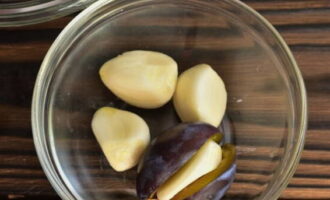 Chop each plum. Remove the pit and put a clove of garlic in its place.