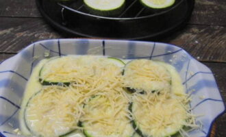 Pour a little sauce into the bottom of the baking dish. Lay out some of the zucchini circles, pour the sauce over again and sprinkle with grated cheese.