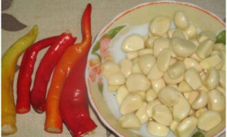 Let's start preparing boiled adjika from tomatoes for the winter with garlic. Peel the garlic cloves. We wash the hot peppers and cut off their tails.