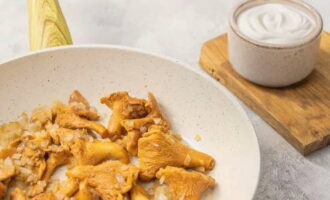 Panaskan mentega dalam kuali dan goreng bawang di dalamnya sehingga perang keemasan. Panaskan chanterelles dalam colander dengan air mendidih, goncangkan cecair yang berlebihan dan pindahkan cendawan ke dalam kuali. Goreng chanterelles dengan api sederhana dengan kacau selama 20 minit.