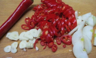 Cortar el pimiento picante en aros. Cortamos la cebolla en mitades finas y el ajo en rodajas.