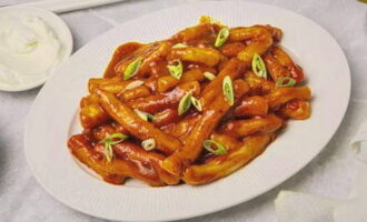 Place prepared Korean-style teokbokki at home into portioned plates, sprinkle with chopped green onions and serve with sour cream. Bon appetit! 