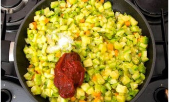 Voeg na 5-7 minuten de courgetteblokjes toe om te bakken, breng de groenten op smaak met kristalsuiker, zout en tomatenpuree. 