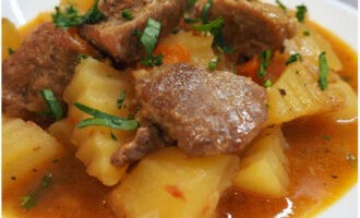 Stewed potatoes with meat in a cauldron on the stove is ready. Place on plates and top with herbs!