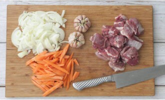 We wash the lamb and cut it into portions. We cut the onion into half rings, and the carrots into cubes. Leave one onion whole.We remove only the top husk from the garlic heads.