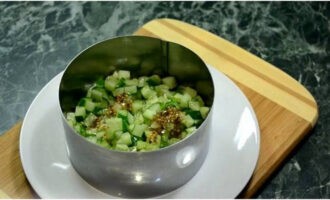 Chúng tôi sẽ thu thập món salad theo từng lớp. Nhưng bạn cũng có thể chỉ cần trộn tất cả các sản phẩm đã cắt nhỏ vào một cái bát. Đặt một vòng phục vụ trên một đĩa phẳng. Đặt dưa chuột vào lớp đầu tiên và đổ nước sốt lên trên.