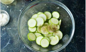 Gebakken courgette in de oven is heel eenvoudig te bereiden. Was de courgette die je hebt geselecteerd om te bakken, droog hem af met een servet en snijd hem in cirkels van maximaal 1 cm dik, het is beter om de dikke schil met een mes te verwijderen. Bestrooi de gesneden courgette met zout en zwarte peper en roer.