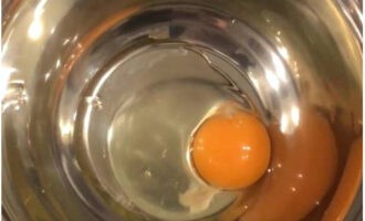 Luftige kefirpannekaker er veldig enkle å tilberede. Ett egg brytes i en bolle for elting av deigen.