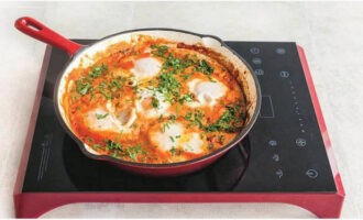 Make holes in the tomato frying according to the number of eggs, break the eggs into them. Cook the shakshuka until the whites are set.