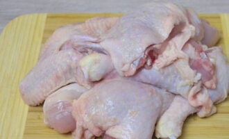 El pollo con patatas al horno se prepara de forma rápida y sencilla. Cortar el pollo en porciones, enjuagar y colocar en un bol.