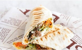 โอน Shawarma โฮมเมดกับไก่ในขนมปังพิต้าใส่จาน ผ่าครึ่งแล้วเสิร์ฟ อร่อย!