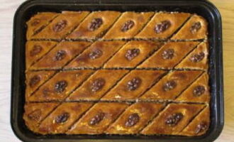 Nadat we de afgewerkte baklava hebben verwijderd, werken we de spleten bij en gieten we siroop over elke diamant. Wanneer het dessert volledig is afgekoeld, maak je sneden helemaal tot aan de bodem.