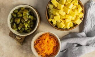 Después de lavar las verduras, pélalas con un pelador de verduras. Cortar las patatas en rodajas grandes. Pica los pepinos encurtidos en cubos. Tres zanahorias en un rallador.